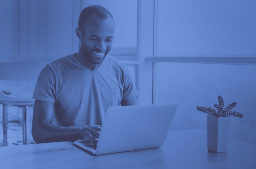man typing on computer with plant on desk