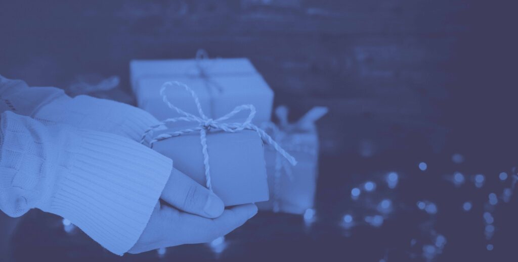 woman holding wrapped present in front of holiday lights